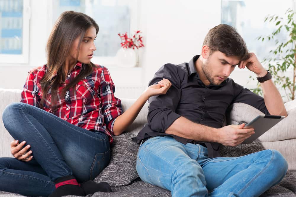 A woman tries getting a man's attention while he is on his phone.