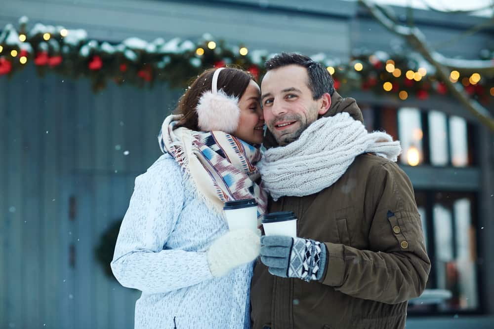 A couple has hot drinks while snuggling close outdoors.