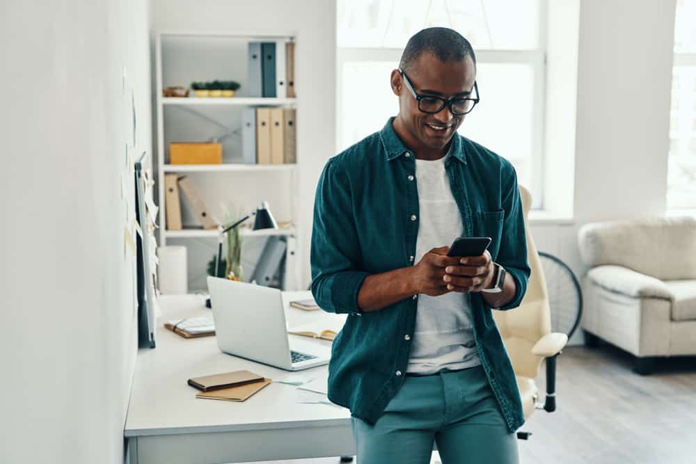 Man smiling in his office while scrolling on his phone. 