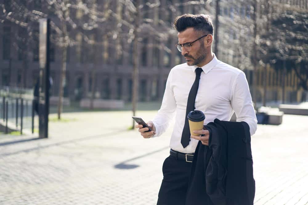 A man in a suit is outside reading a message on his phone.