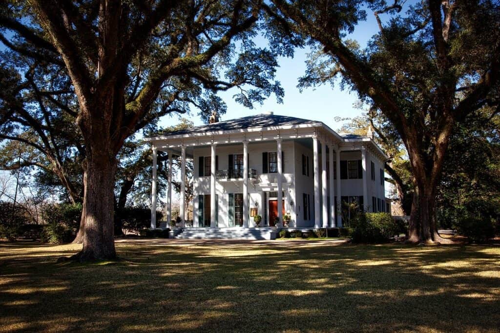 A plantation-style house on an estate sits in the shade of surrounding trees.