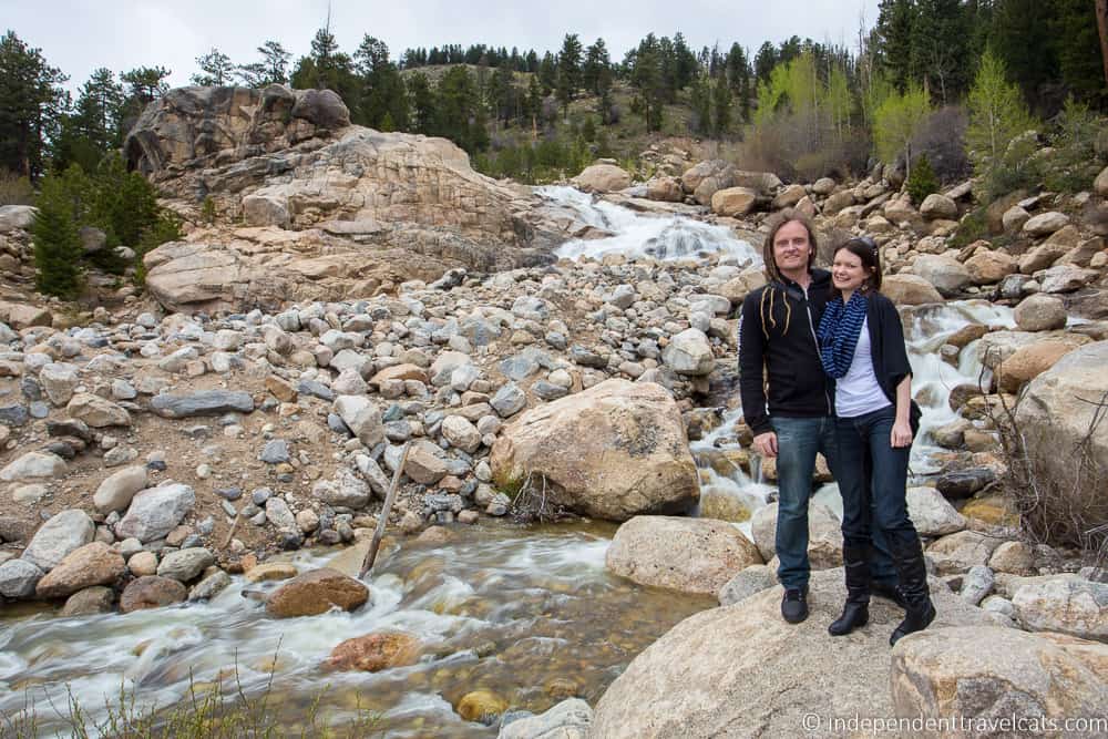 Two people standing on a rock next to a small river.