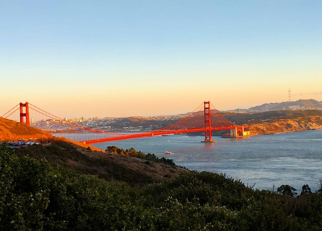 View of the Golden Gate Bridge from a viewpoint atop a hill in the distance at sunset.