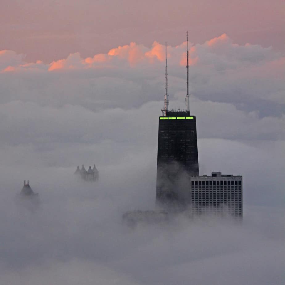 The tops of skyscrapers cutting through the clouds at sunset.