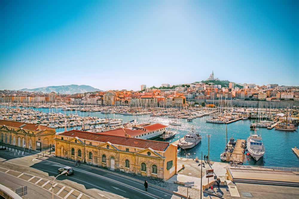 Boats float on a harbor by an empty street under a blue sky.