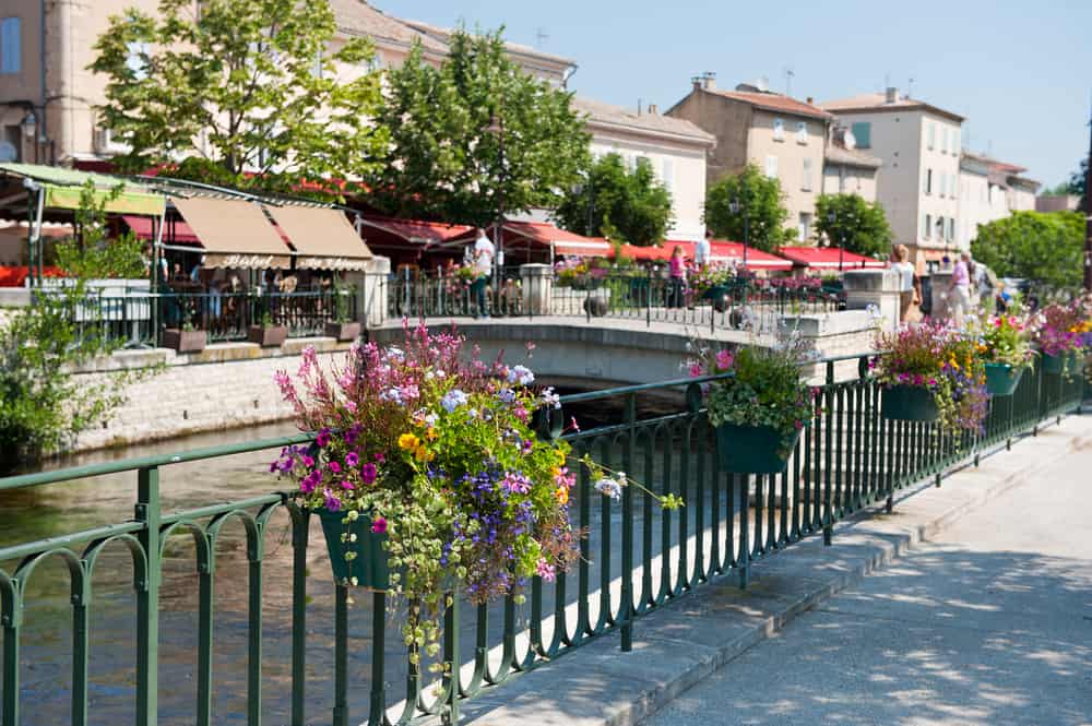 Railing with flowerpots hanging along the edge leading to a bridge over a small river. 