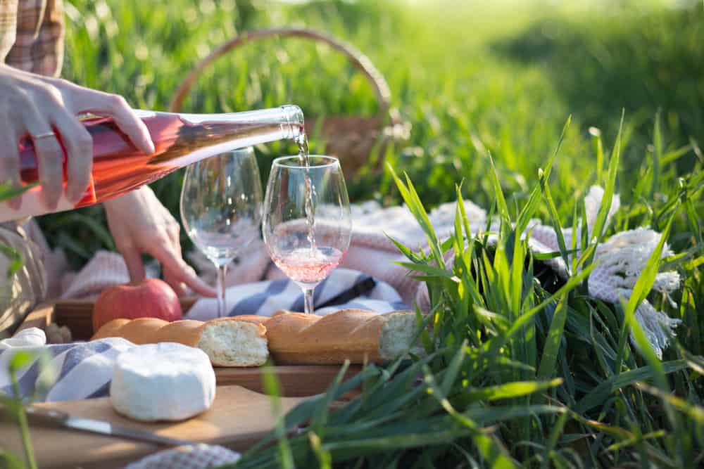 Rose wine being poured into a glass next to cheese and bread surrounded by glass.
